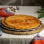 Empanada gallega artesanal entera sobre plato tradicional, masa dorada y horneada a mano