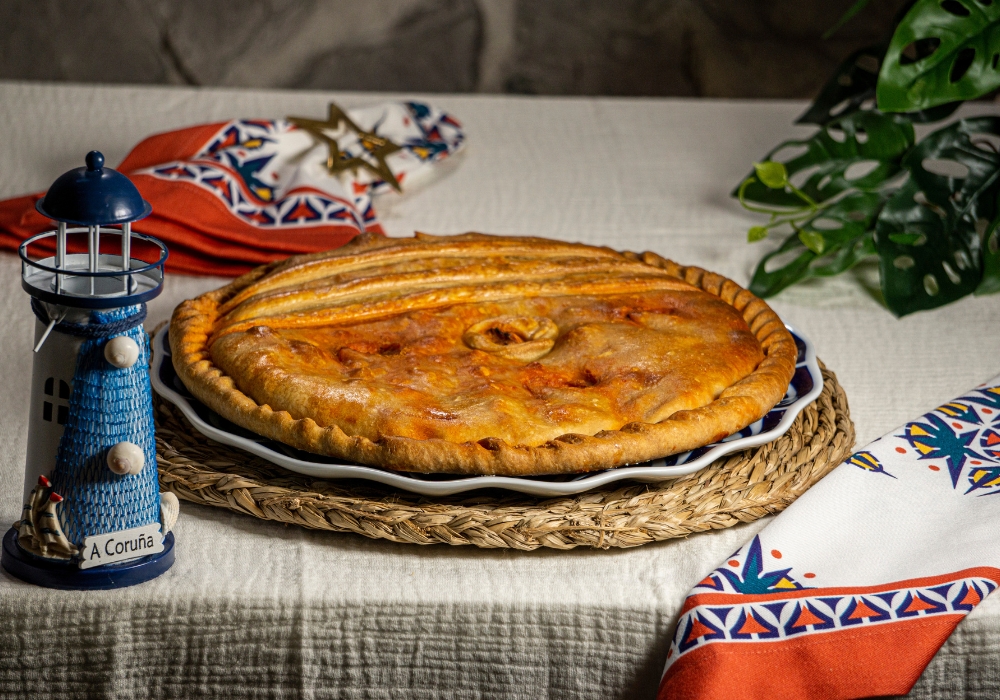 Empanada gallega artesanal entera sobre plato tradicional, masa dorada y horneada a mano